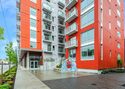 Entrance to 900 Rainier with red facade, glass doors, landscaped sidewalk, and public art sculpture.