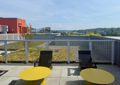 Rooftop deck at 900 Rainier with outdoor seating, yellow tables, and city skyline views.